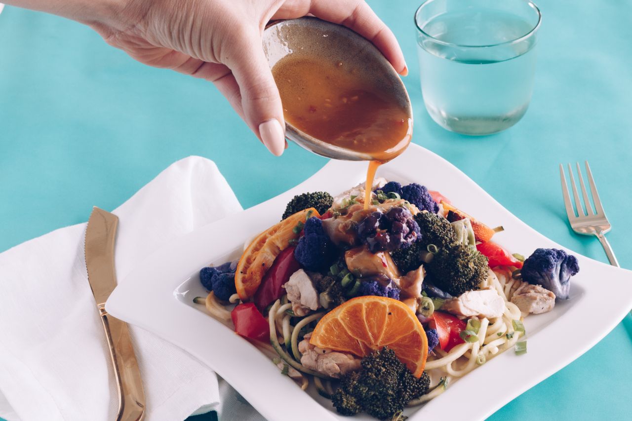 Healthy dish with veggies and sauce being poured on noodles, showcasing bright colors.